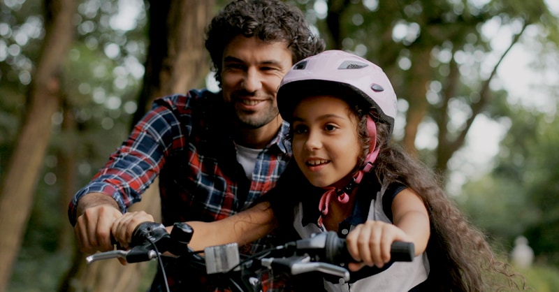 Niña disfruta de andar en bicicleta junto a su padre. 