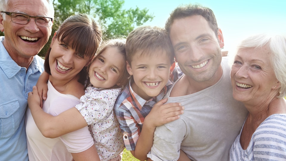 Un grupo de seis personas, entre adultos y niños, sonriendo al aire libre en un entorno soleado con vegetación de fondo.